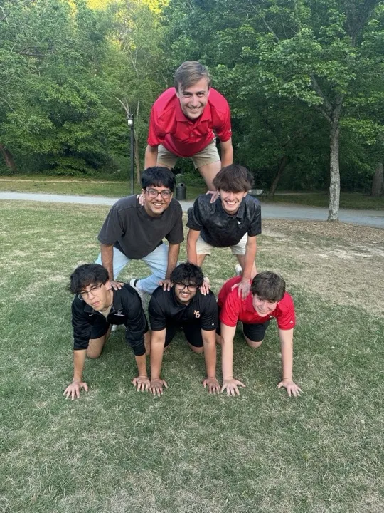 Six friends in a human pyramid on a lawn